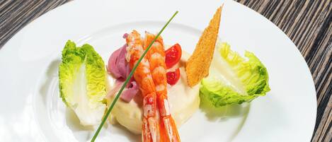 Un plato blanco con un guiso de mariscos, incluyendo camarones, tomates cherry y una guarnición.