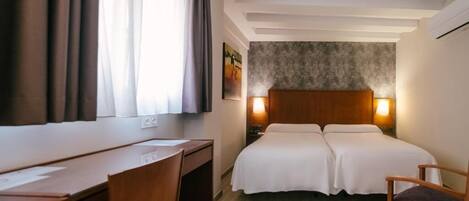 Una habitación de hotel con cama, escritorio, silla y ventana con cortinas.