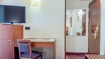 Una habitación de hotel con cama, escritorio con silla, televisor y armario.