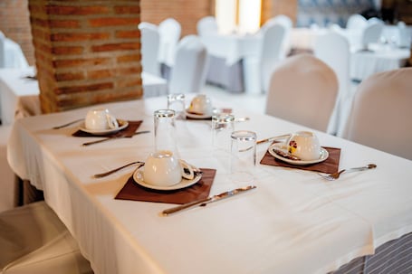 A dining table set with white tablecloths, white chairs, and neatly arranged cutlery and glassware.