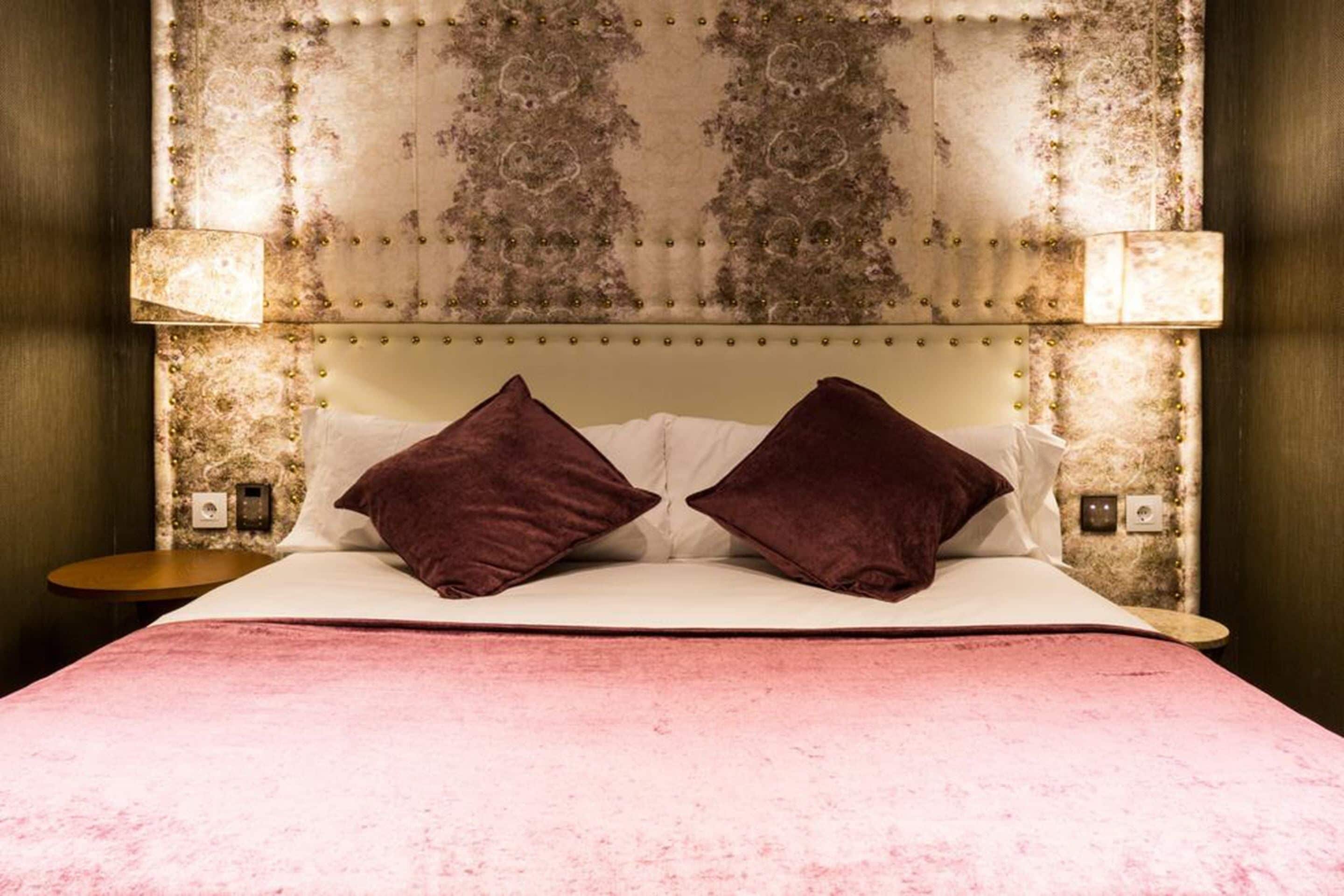 A bed with a tufted headboard, two pillows, and a pink bedspread.
