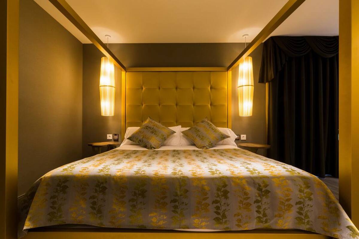 A large bed with a tufted headboard, two bedside lamps, and a floral-patterned bedspread.