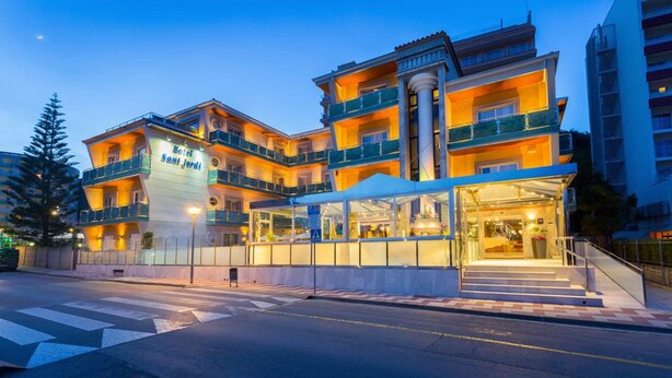 Un hotel de varios pisos con una entrada destacada, balcones y una vista despejada de la calle.