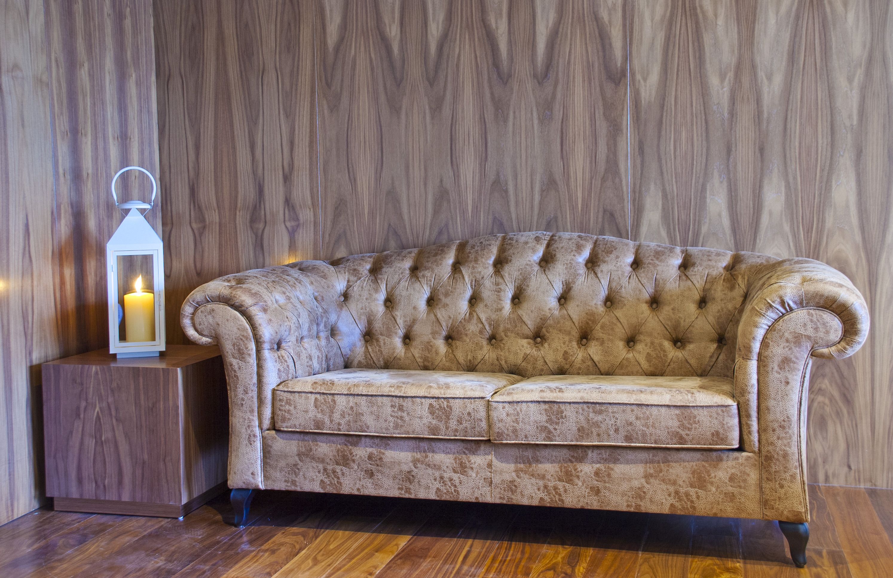 A tufted sofa with a wooden side table and a lit candle in a wooden-paneled room.