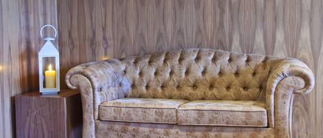 A tufted sofa with a wooden side table and a lit candle in a wooden-paneled room.