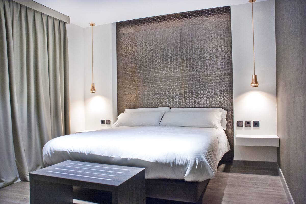 A modern hotel room with a large bed, a bedside table, and a wall-mounted light fixture.