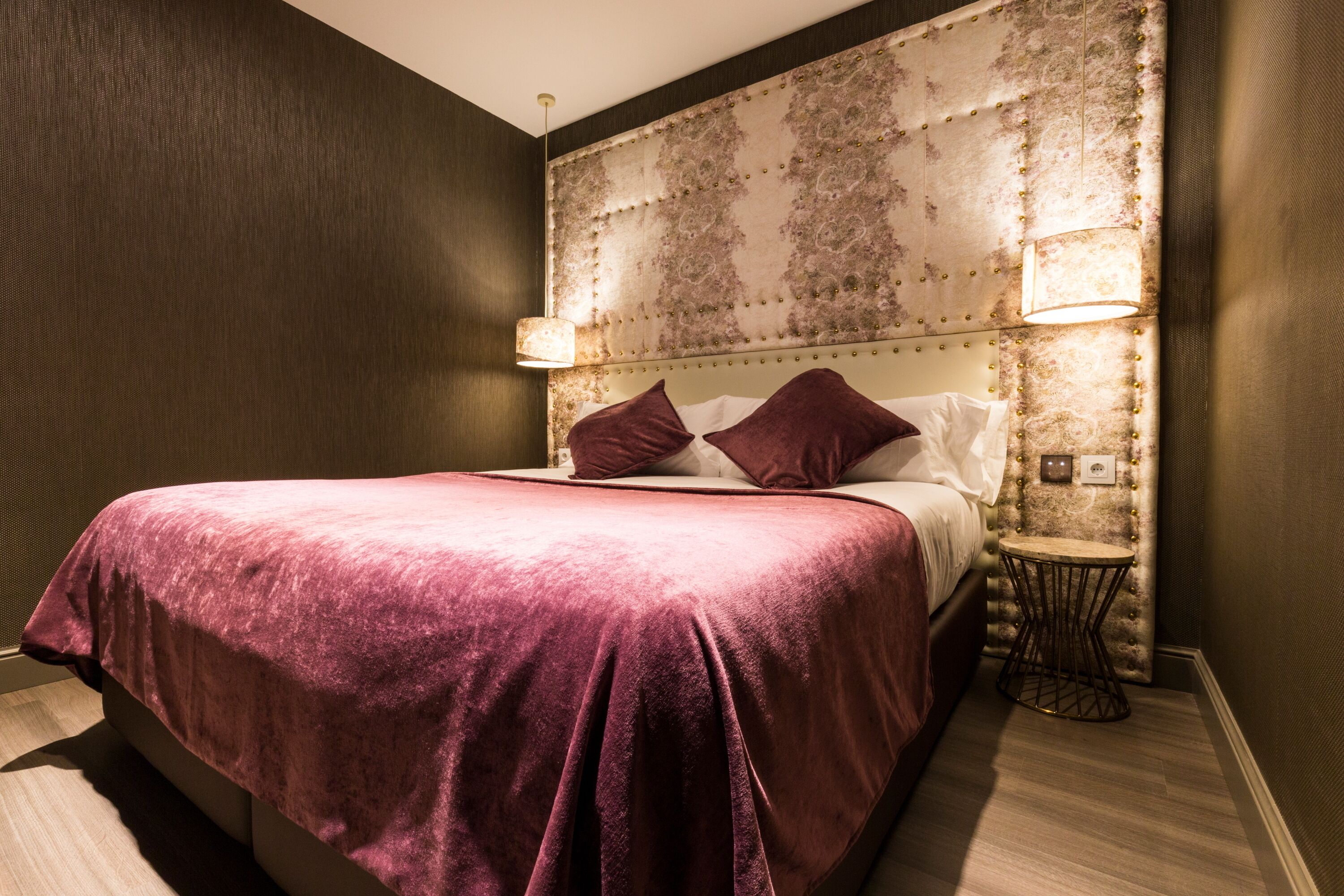 Habitación de hotel con una cama grande, un cabecero decorativo, dos lámparas de noche y una mesita redonda.
