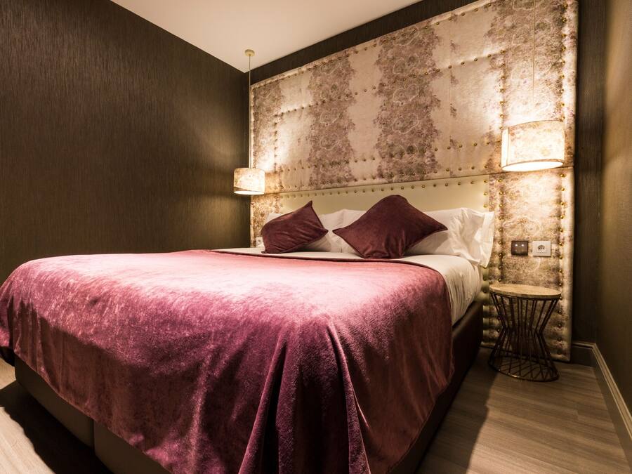 Habitación de hotel con una cama grande, un cabecero decorativo, dos lámparas de noche y una mesita redonda.