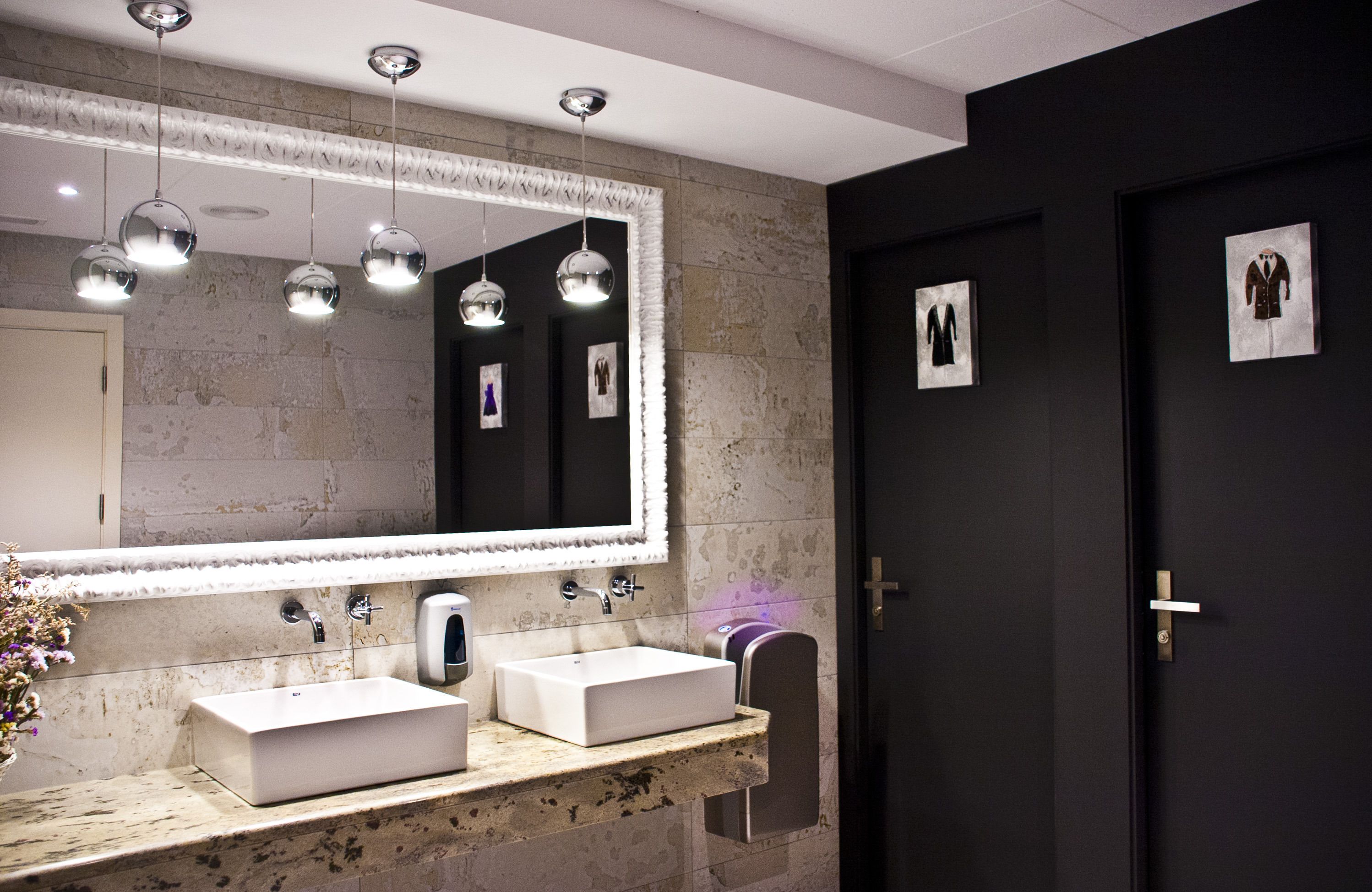 Un baño moderno con un espejo grande, dos lavamanos e iluminación colgante.