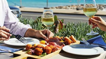 Une table à manger dressée avec une variété de plats et deux verres de vin blanc, le tout mis en valeur par une vue panoramique sur l’océan.