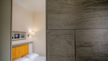 Una habitación de hotel con cabecera de madera, cama con ropa blanca e iluminación fijada a la pared.