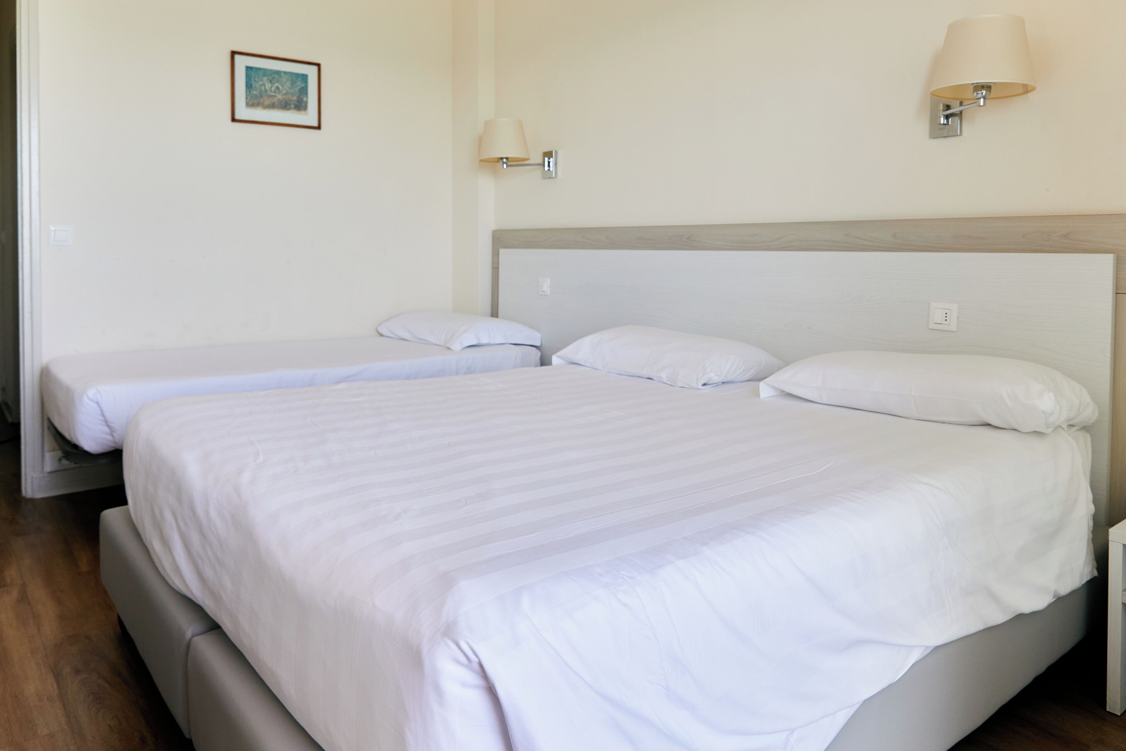 Una habitación de hotel con una cama grande, dos camas más pequeñas y dos lámparas fijadas a la pared.