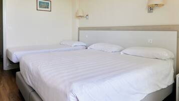 Una habitación de hotel con una cama grande, dos camas más pequeñas y dos lámparas fijadas a la pared.