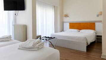 Habitación de hotel con dos camas, un televisor montado en la pared, un radiador y una ventana con cortinas.