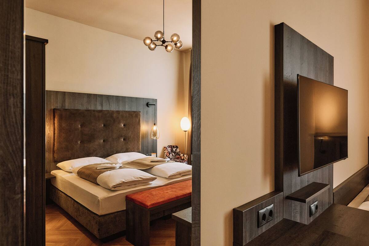 Une chambre moderne avec un grand lit, des lampes de chevet, un banc et un téléviseur fixé au mur.