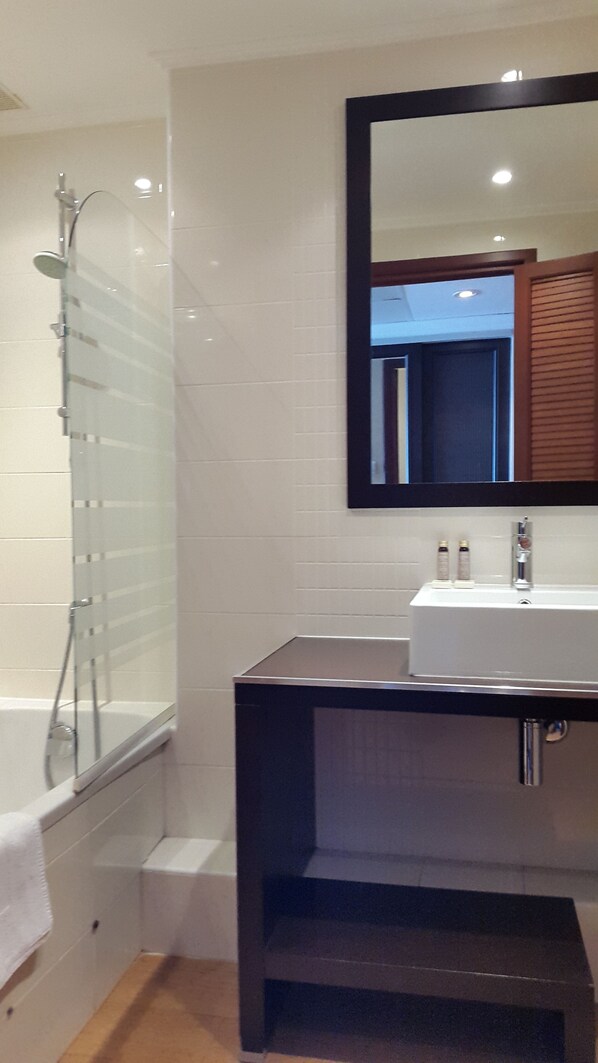 Une salle de bain moderne avec une douche à l’italienne en verre, un lavabo blanc doté d’un plan de toilette foncé et un grand miroir au-dessus du lavabo.
