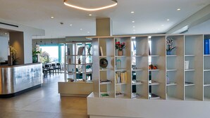 A modern reception area with a reception desk, a seating area, and a bookshelf with various items. - Princess et Richmond (Menton)