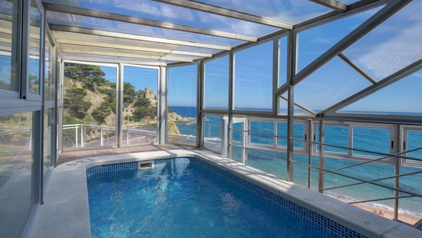 Una piscina infinita con paredes de vidrio y vistas despejadas al océano y un paisaje rocoso.