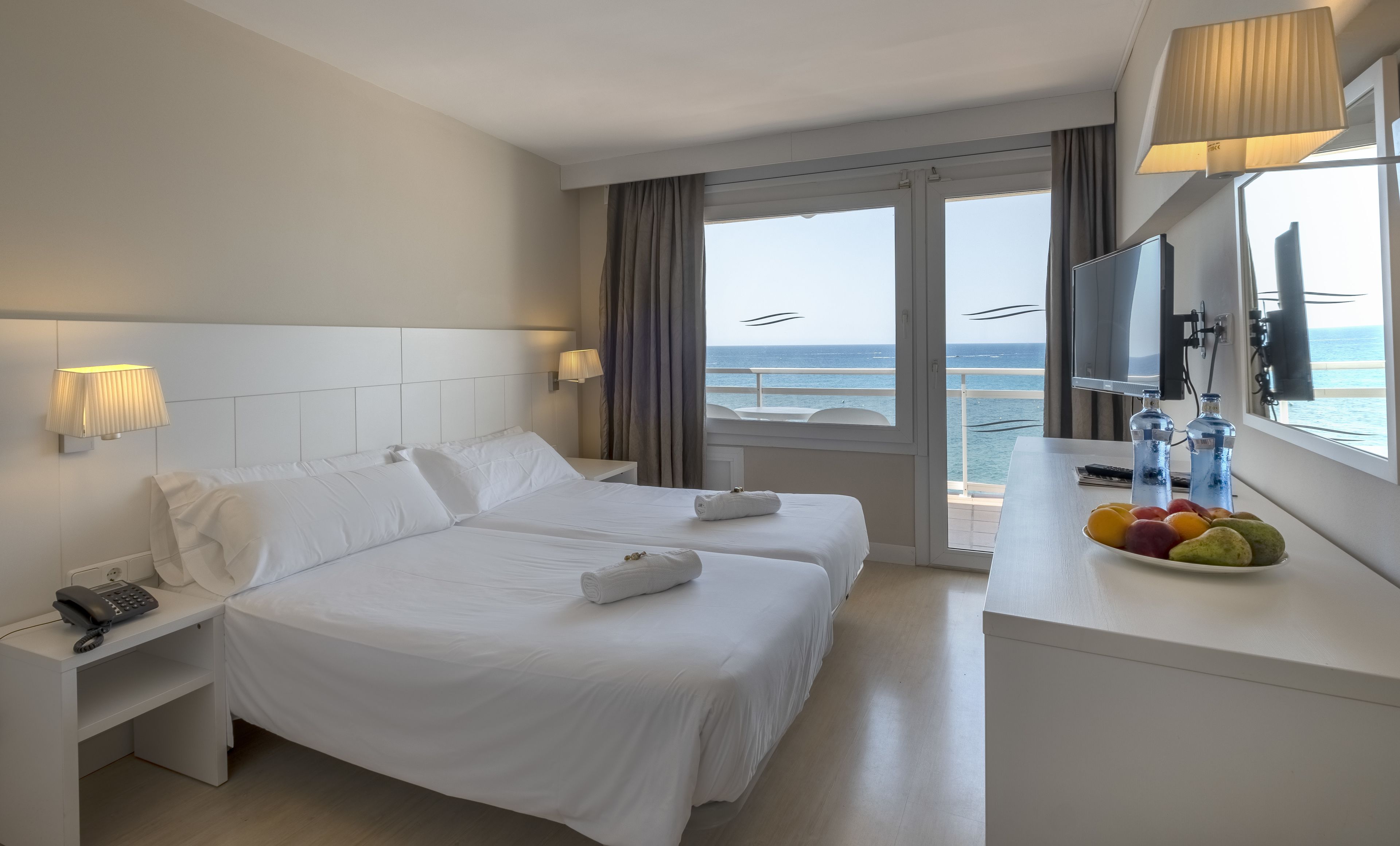 Habitación de hotel con dos camas, un escritorio con fruta, un teléfono y un televisor.
