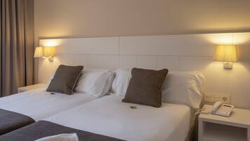 A hotel room with two beds, each with white linens and brown pillows. There are bedside lamps and a phone on a nightstand.