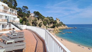 Un hotel frente a la playa con terraza, sillas de descanso y vistas al mar y un castillo.