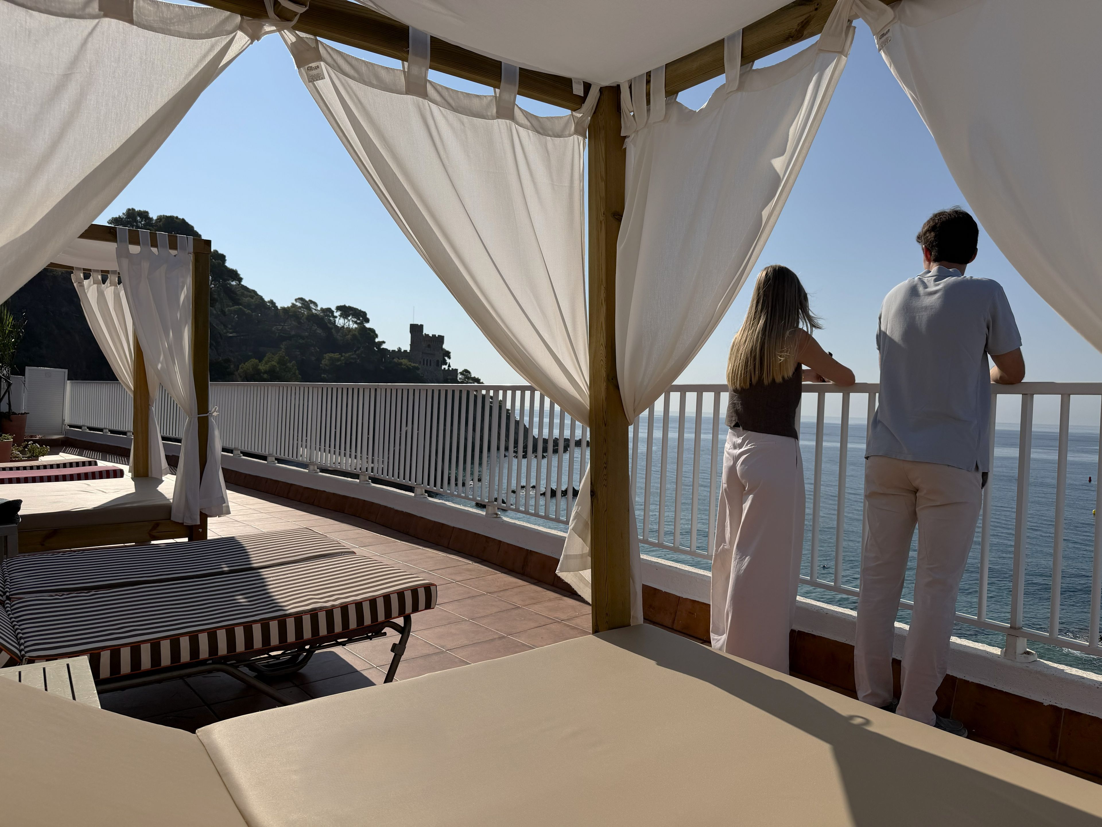 A balcony with a view of the sea, a white canopy, and a wooden railing.