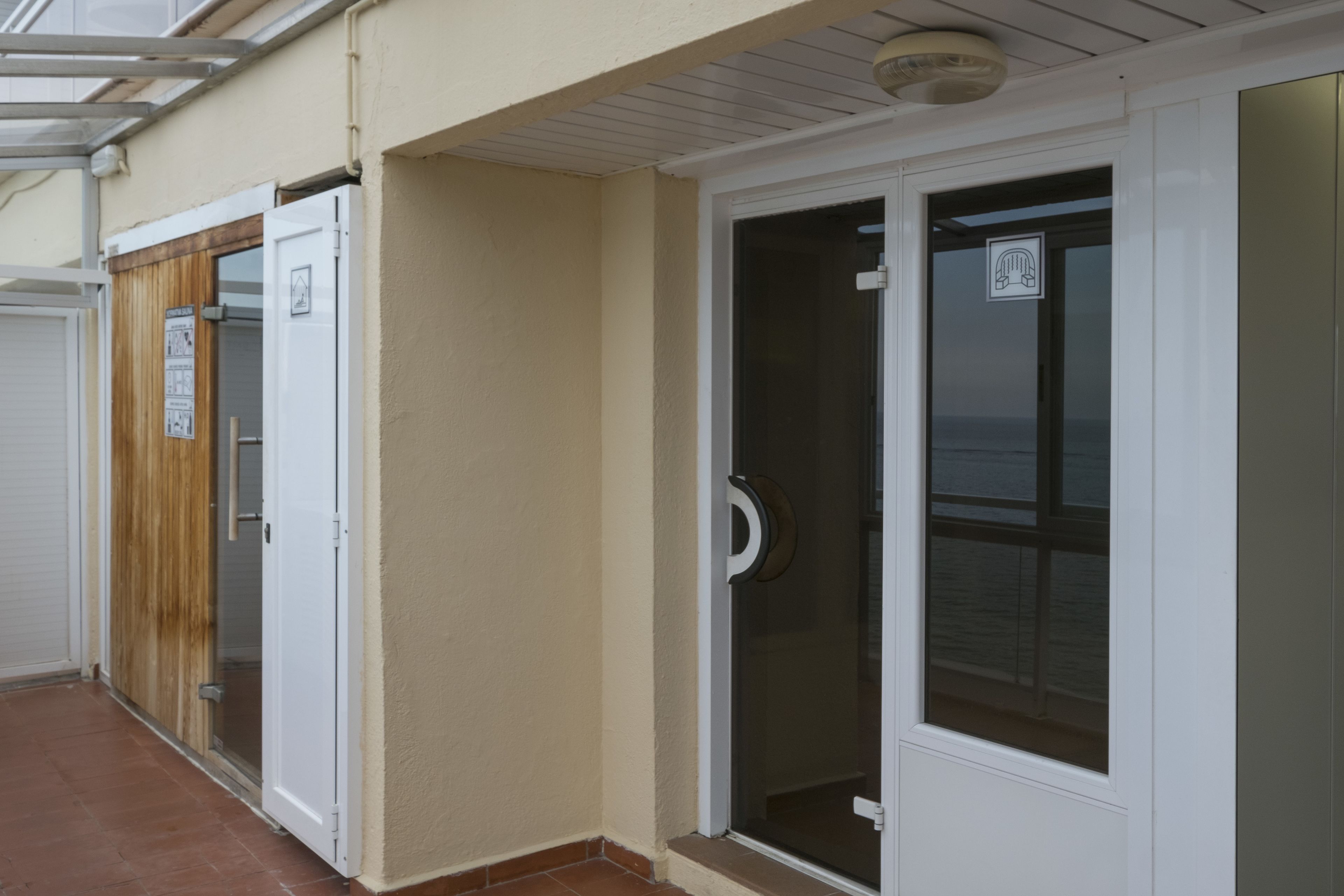 A corridor with a wooden door, a glass door with a hand symbol, and a white door with a window.