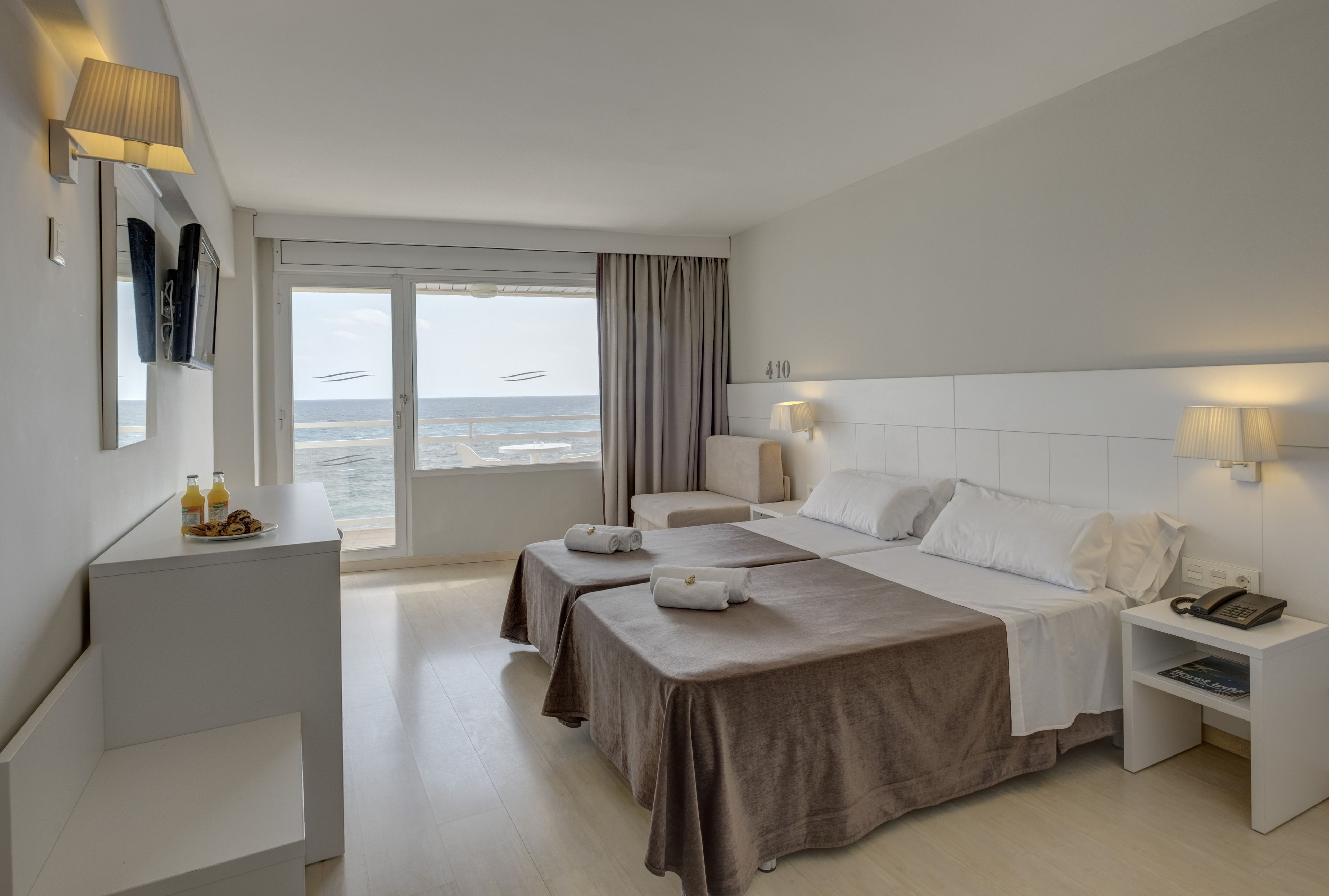 Une chambre d’hôtel avec un lit, deux tables de chevet, un bureau et une vue sur la mer.