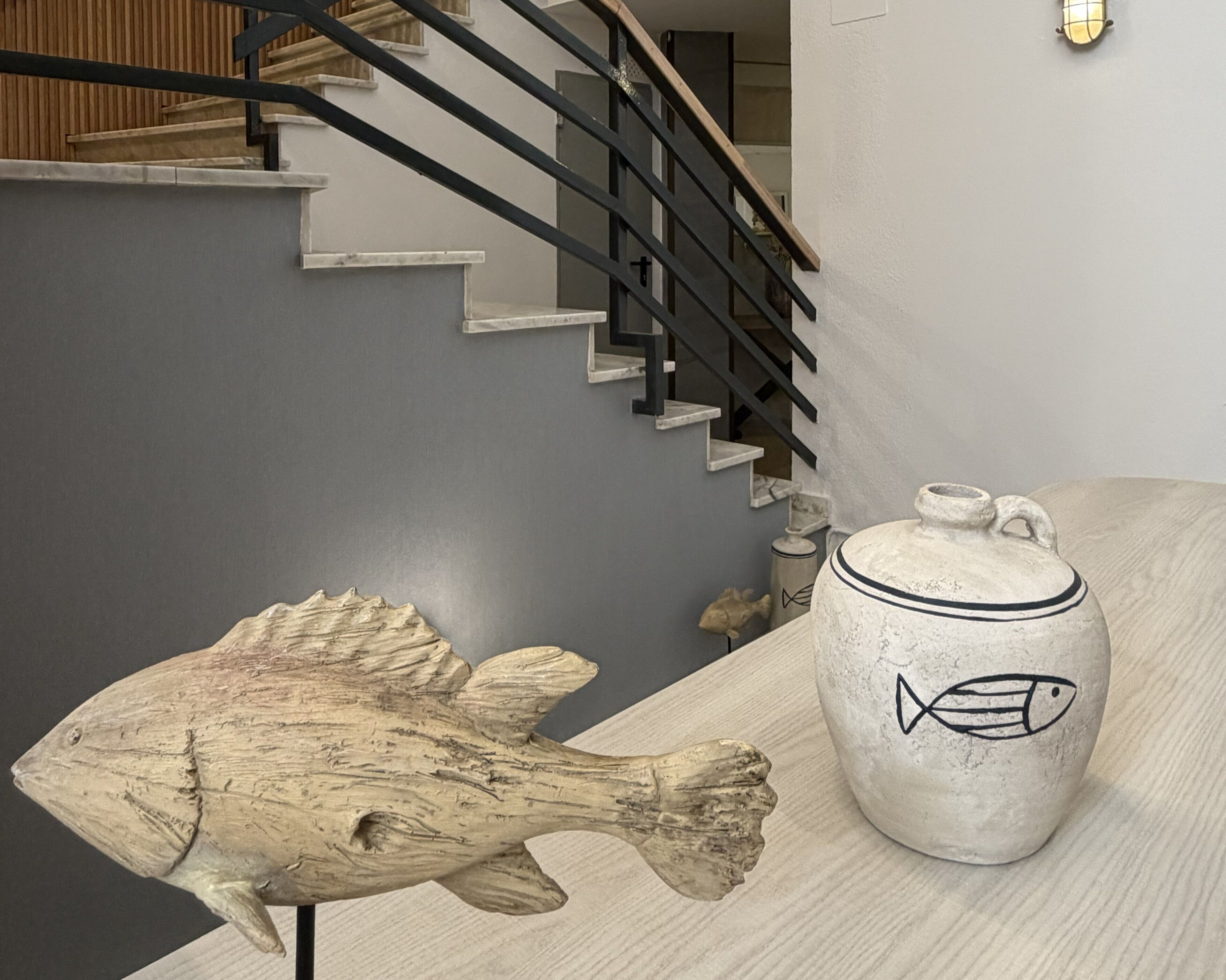 Un interior moderno con una escalera, una escultura de pez de madera y una maceta de cerámica con diseño de pez.