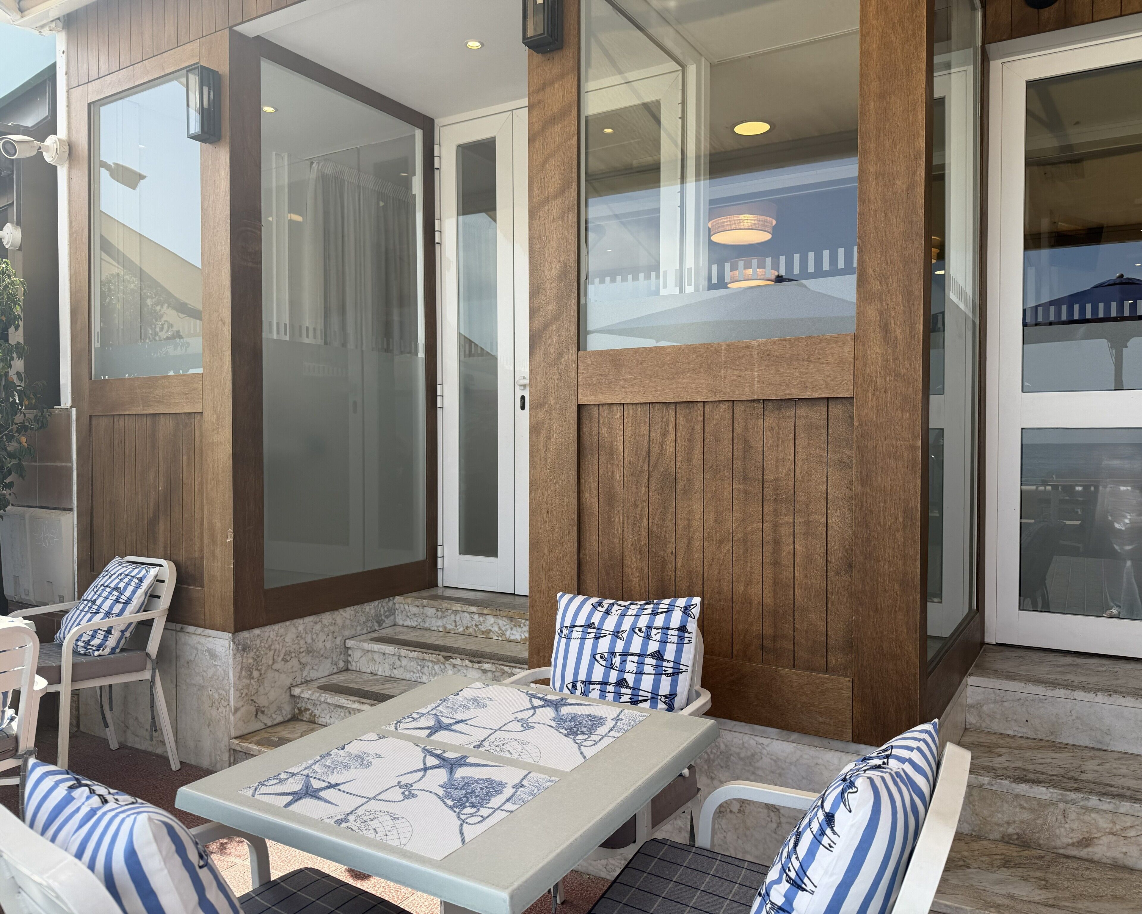 An outdoor patio with a table and chairs, wooden paneling, and glass doors.