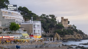 Un hotel costero con un castillo en un acantilado, comedor al aire libre y vistas al mar.