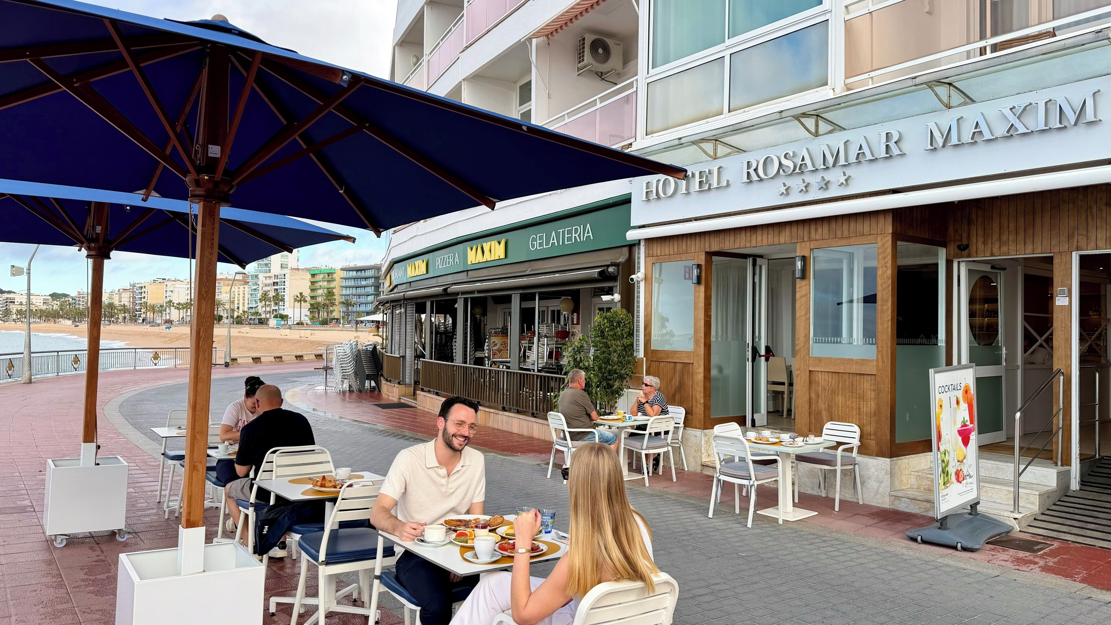 An outdoor dining area with tables and chairs, a covered seating area, and a view of the beach.