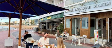 An outdoor dining area with tables and chairs, a covered seating area, and a view of the beach.
