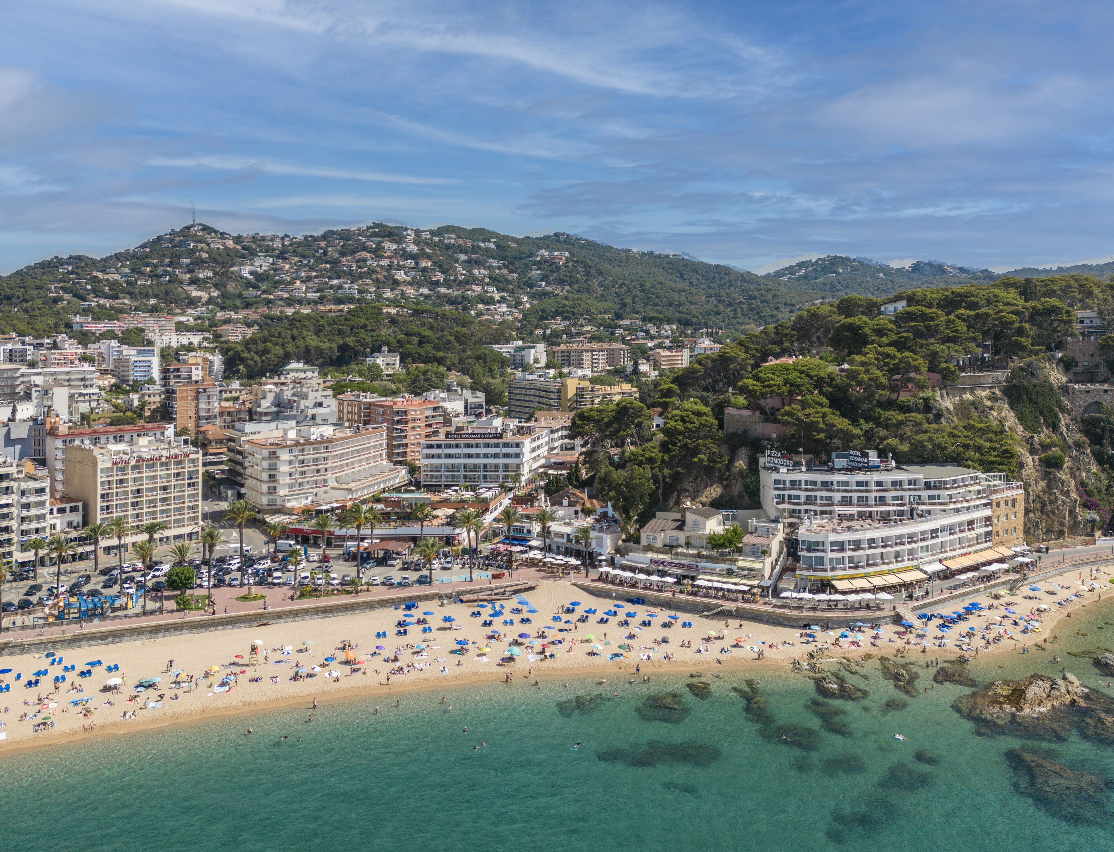 A coastal cityscape with a beach, hotels, and a mountainous backdrop.
