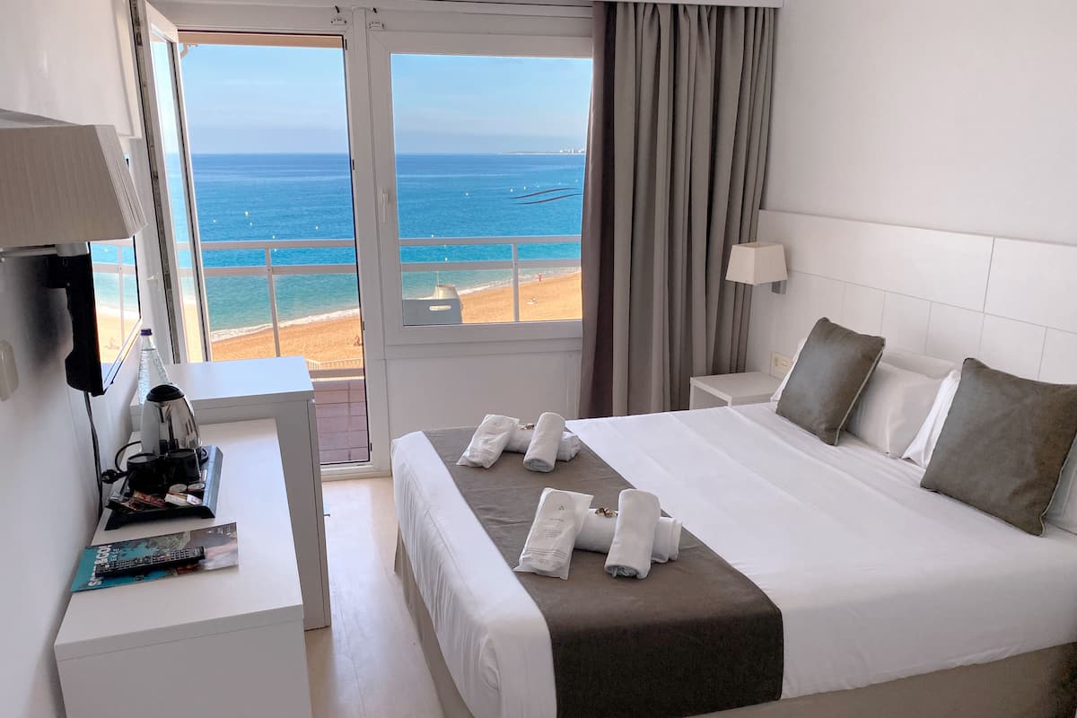 A hotel room with a bed, a desk, a coffee maker, and a view of the beach.