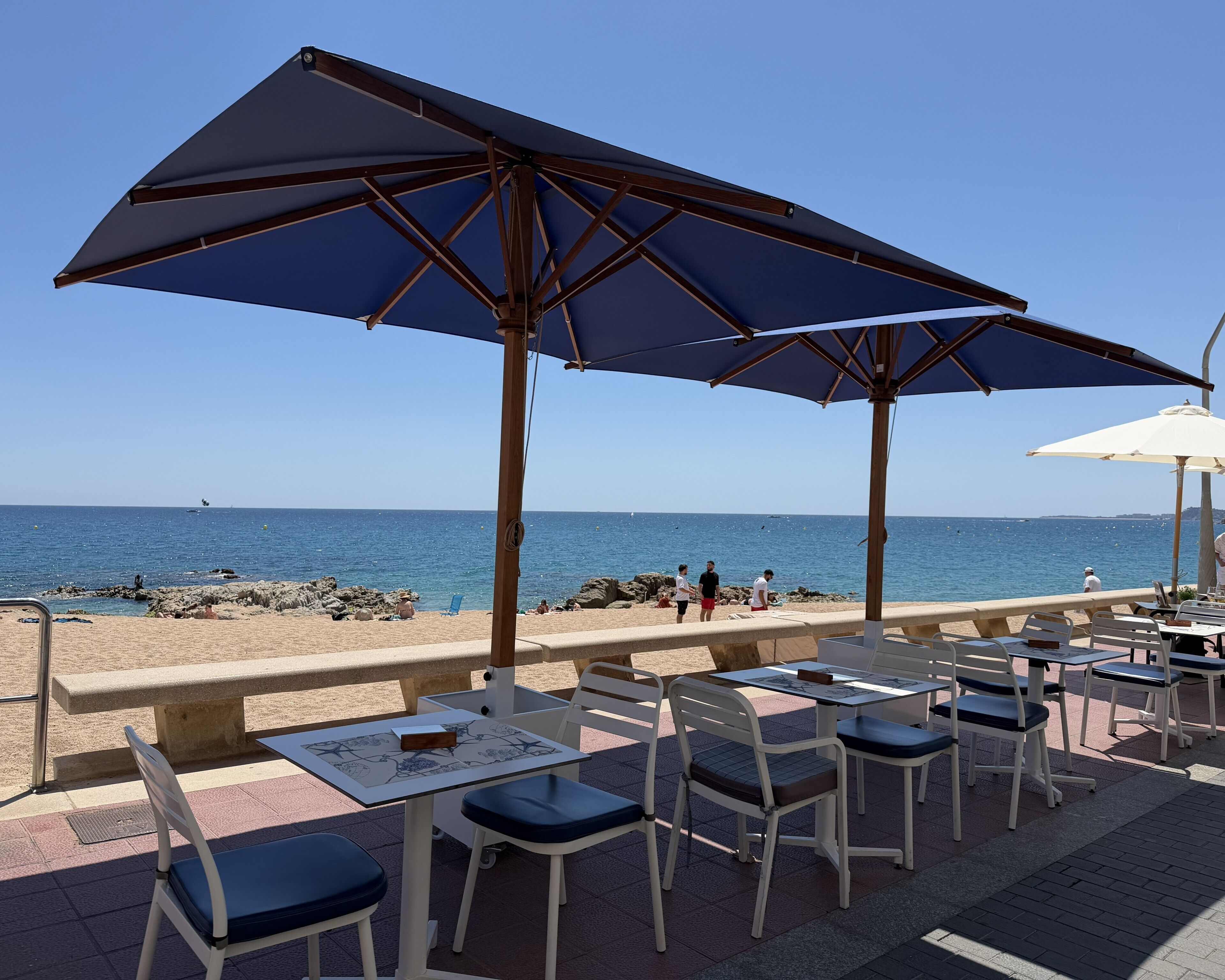 Buiten zitplaatsen met parasols, uitzicht op zee en een rotsachtige kustlijn.
