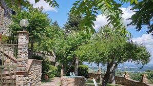 A stone building with a stone wall and gate, a circular stone bench with a swing, and a view of the landscape. - Hotel Pescille by Double Hospitality (San Gimignano)
