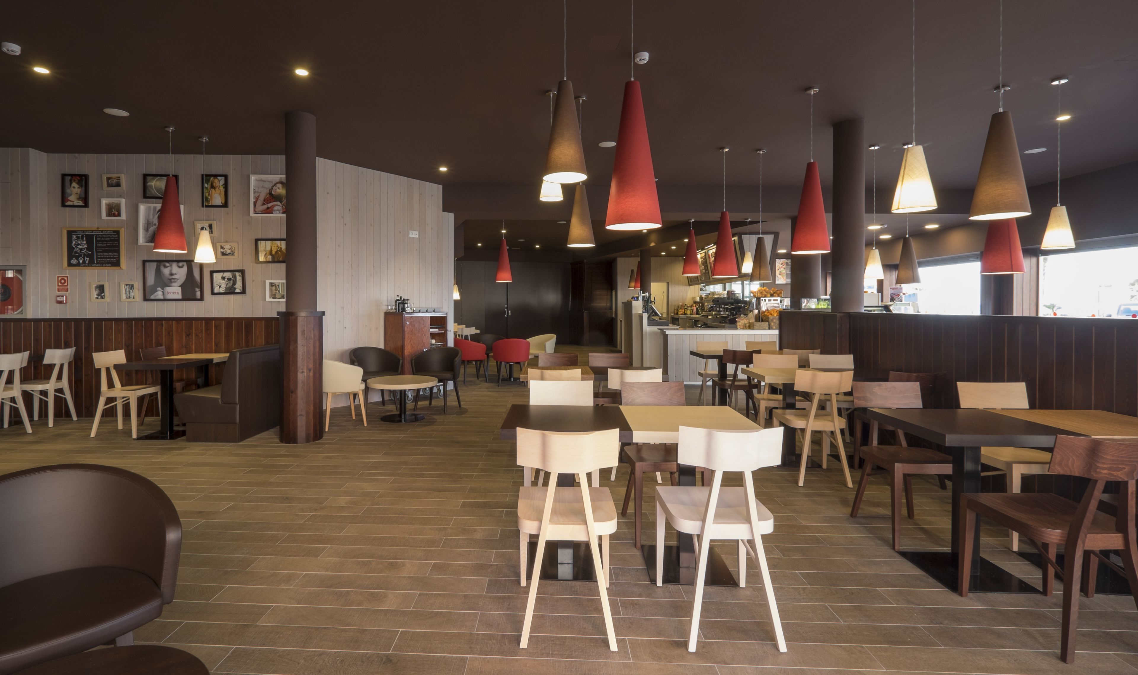A modern restaurant interior with wooden flooring, multiple seating areas, and pendant lighting.