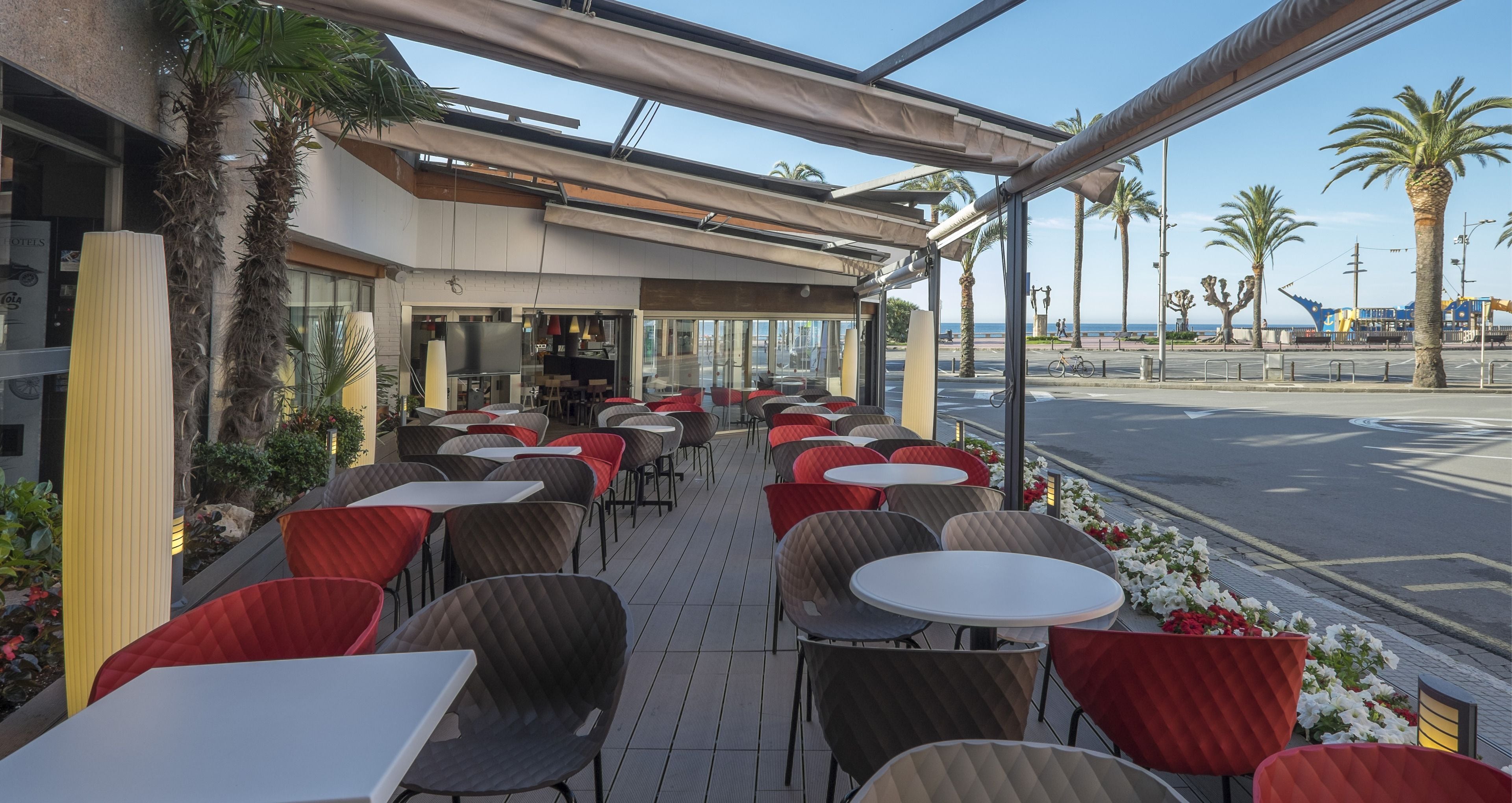 Un café en plein air avec des tables et des chaises, un bâtiment abritant un restaurant et des palmiers.