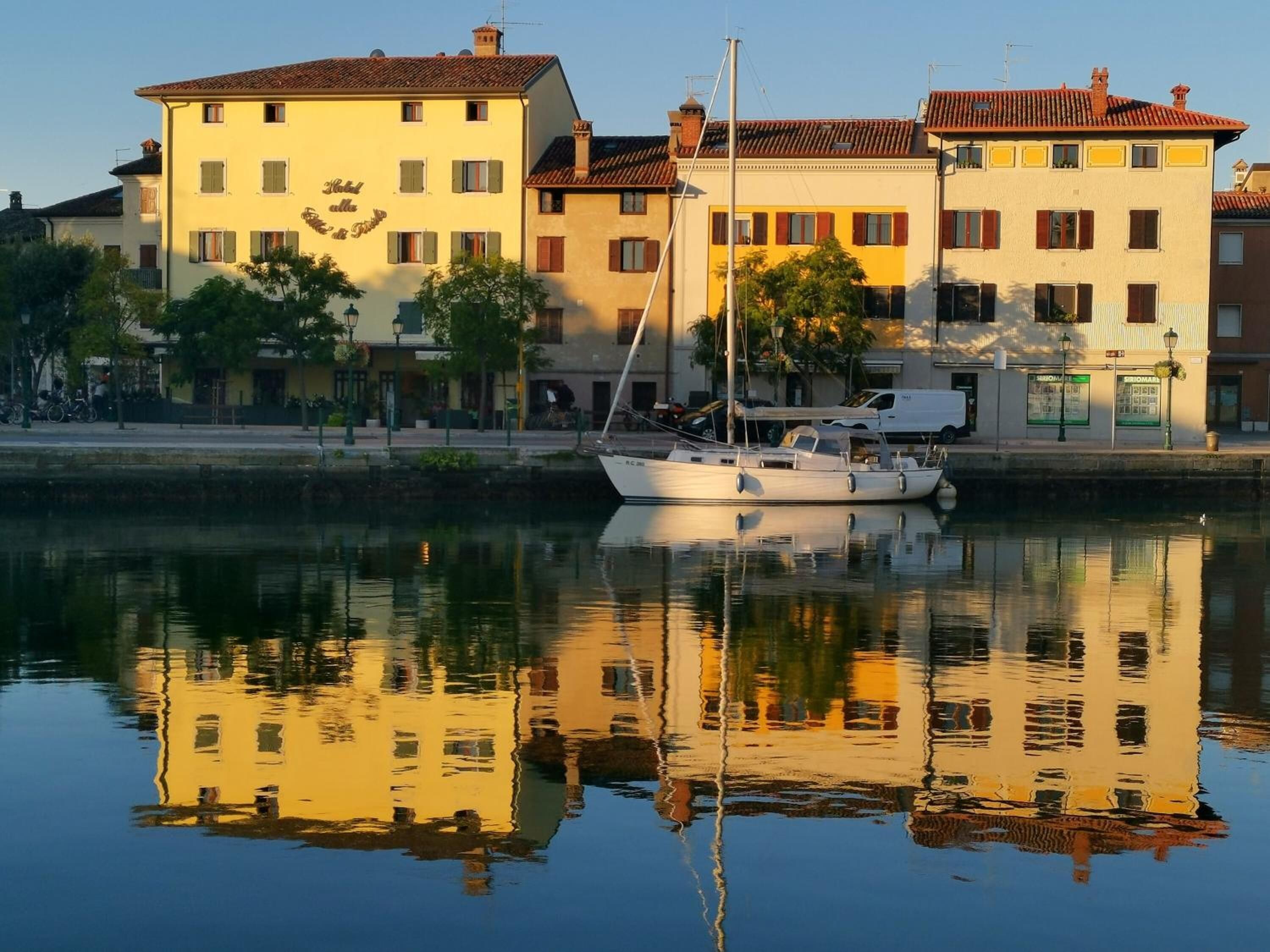 Un canal con un velero blanco amarrado, edificios con balcones y un cielo despejado.