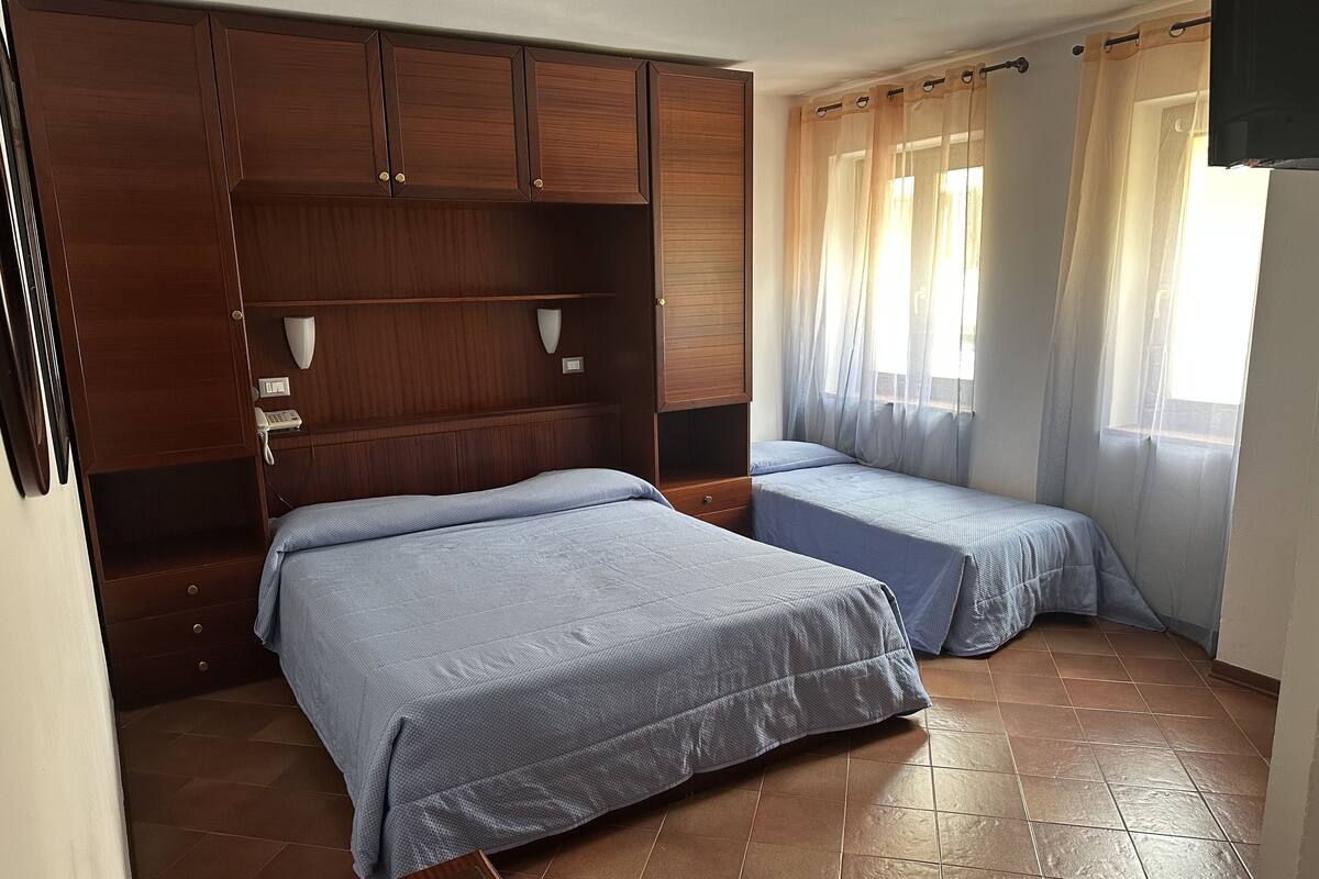 A bedroom with two beds, wooden wardrobe, and a window with curtains.
