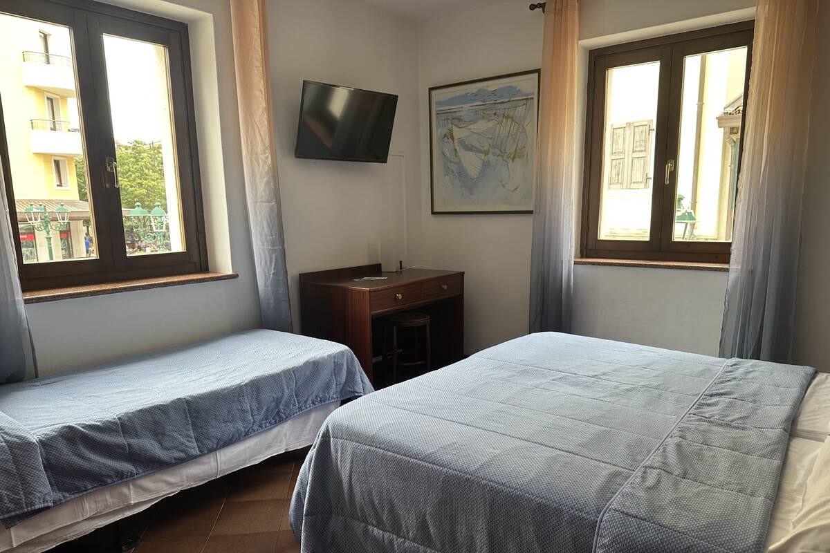 A room with two beds, a desk, a TV, and large windows.