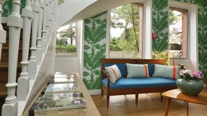 Una escalera con balaustres blancos, un sofá azul con cojines a rayas y un florero con flores sobre una mesa de madera.