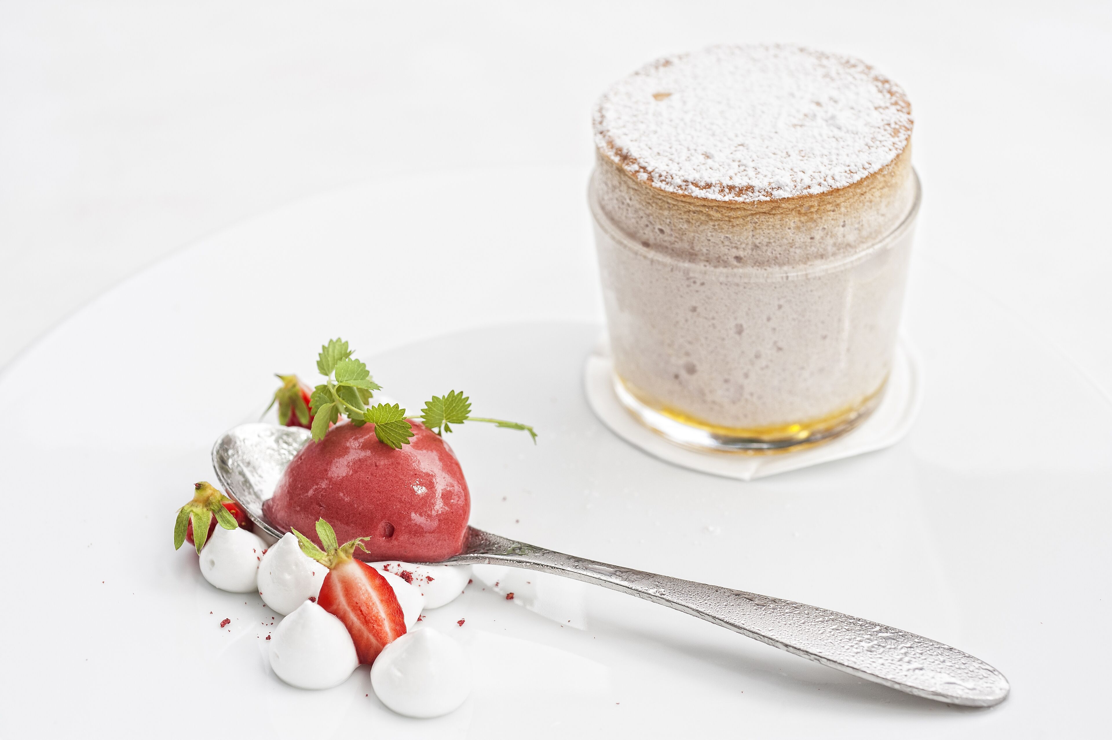 A dessert with a scoop of ice cream and a glass of a creamy beverage, garnished with strawberries and mint leaves.