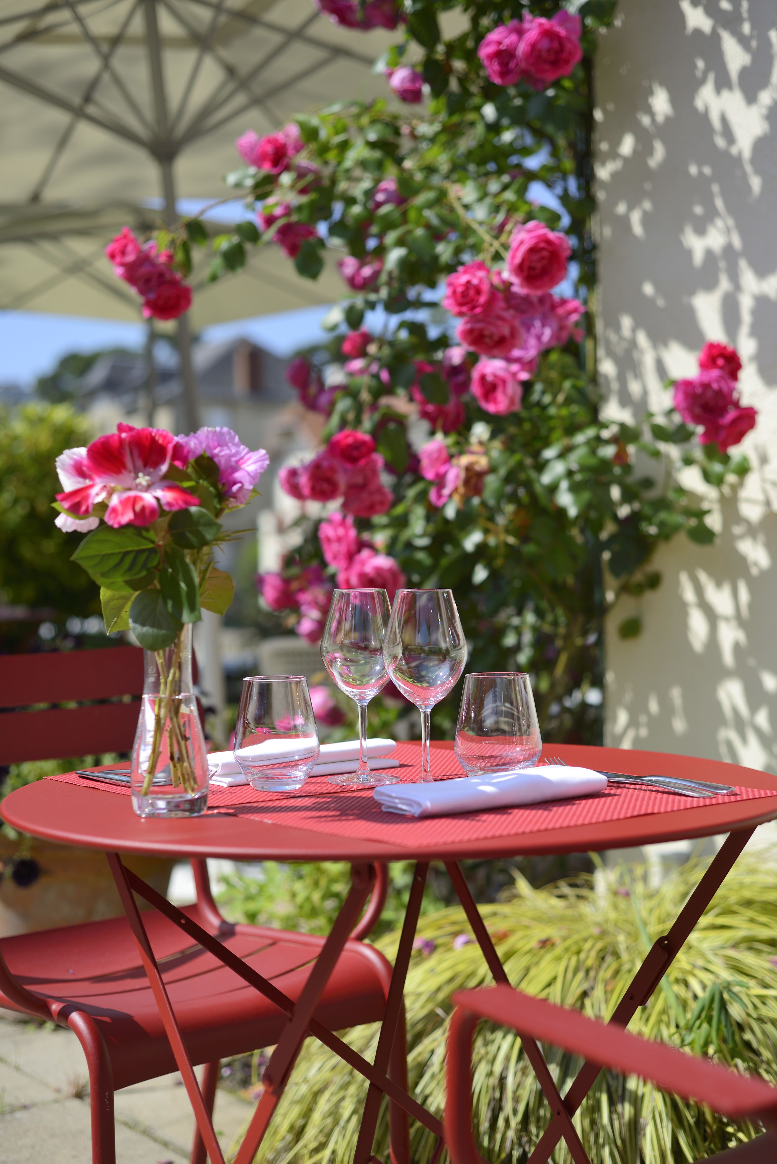 Una mesa metálica roja con copas de vino, un florero con flores y una servilleta.
