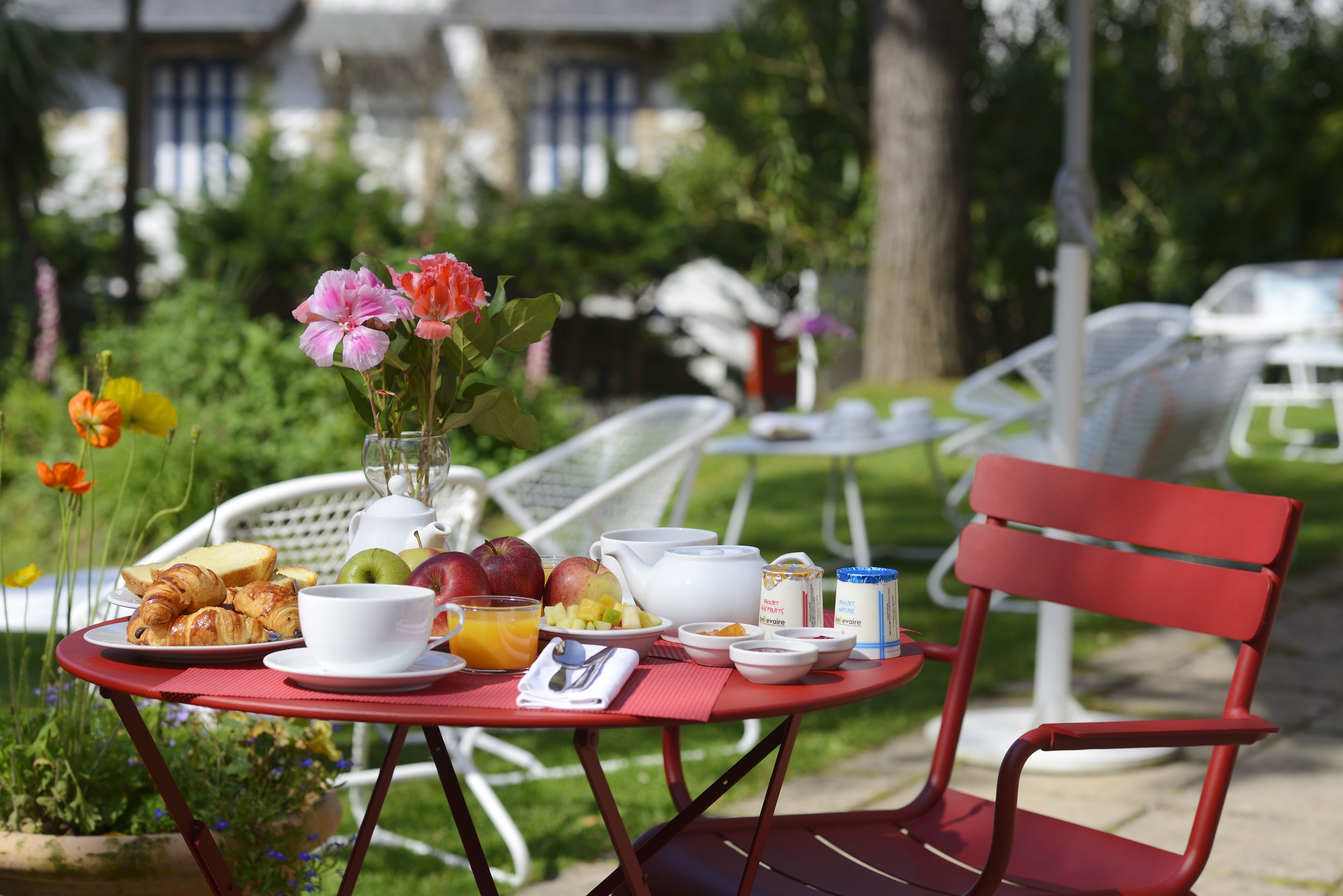 A red table with breakfast items including croissants, fruit, and a vase of flowers.