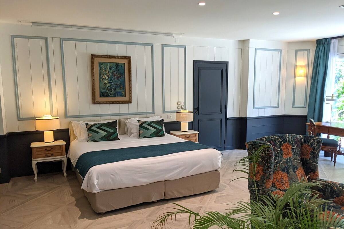 A hotel room with a large bed, two bedside tables with lamps, a dark door, and a view of the outdoors.