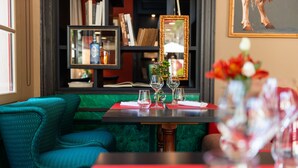 Un comedor con una mesa preparada para dos, una silla tapizada en color verde azulado y una estantería al fondo.