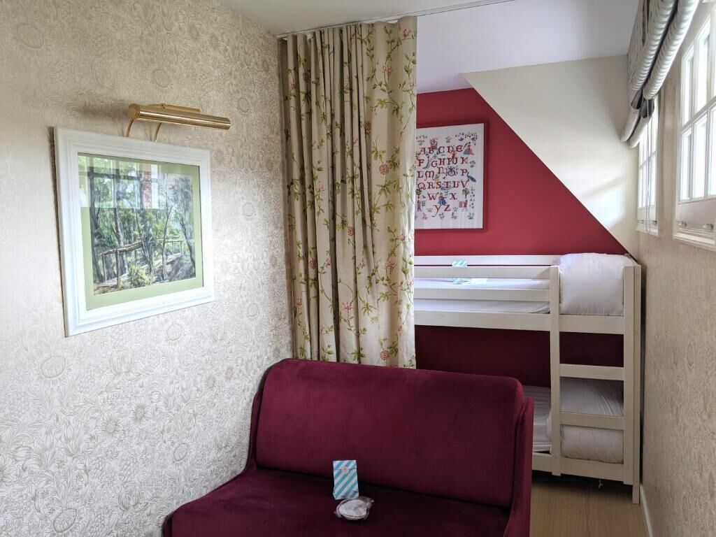 A room with a red wall, a bunk bed, a framed picture, and a window with curtains.