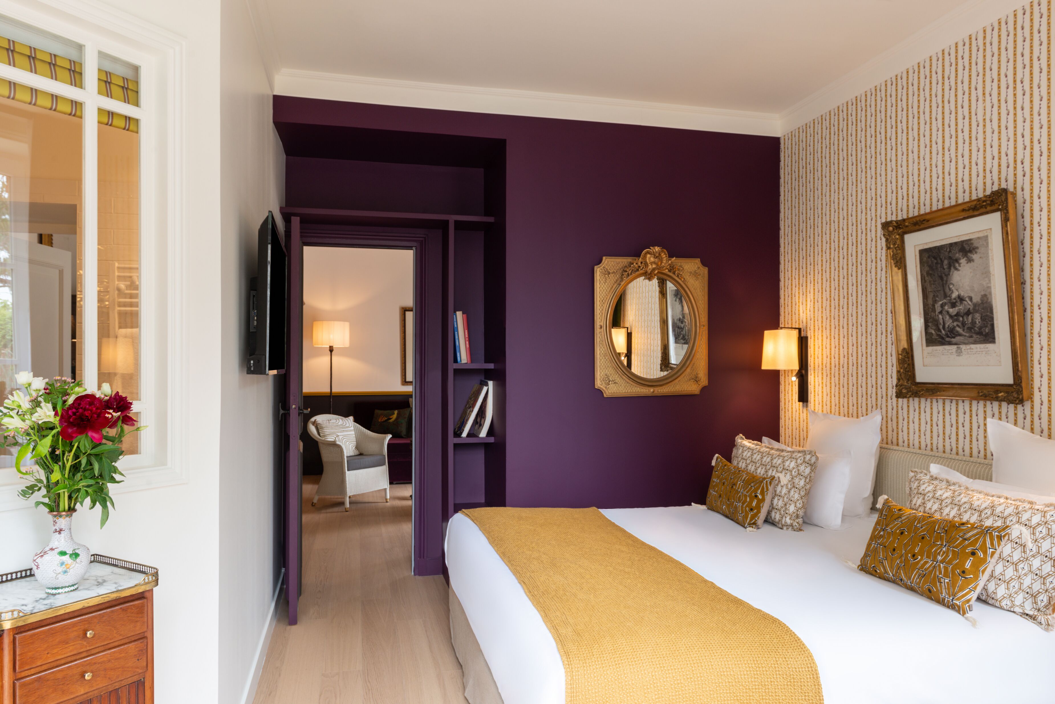 Een hotelkamer met een groot bed, een paarse accentmuur, een spiegel en een ingelijst kunstwerk.